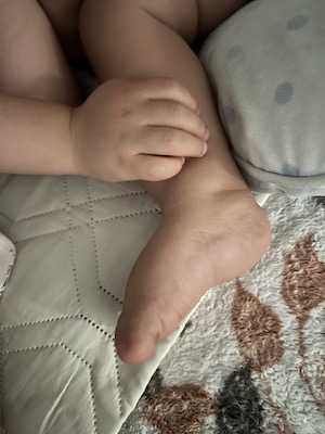 Baby's hand lying on another baby's leg.